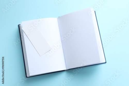 Book with white bookmark on light blue background, top view. Space for text