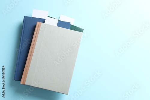 Books with white bookmarks on light blue background, top view. Space for text