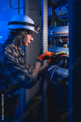 Female electrician installing wiring in electrical panel. Industrial maintenance work