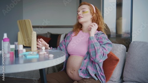 Pregnant woman sitting at a table with makeup and beauty products in a modern living area during daytime