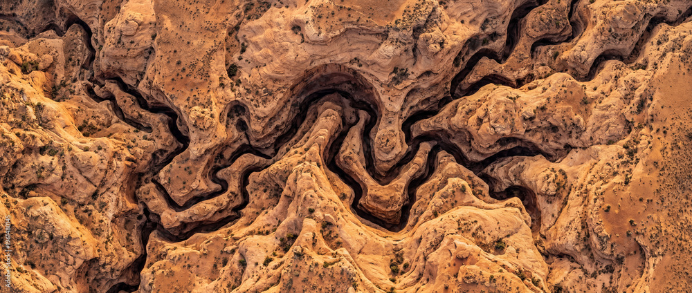 Obraz premium Vertical aerial of sculpted desert sandstone carved into swirling ravines and tight channels, revealing an intricate maze of eroded rock textures, warm earth tones, and abstract geology