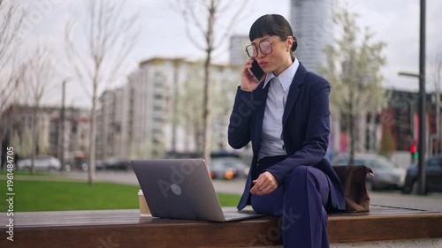 Businesswoman on phone with laptop and coffee in urban park setting