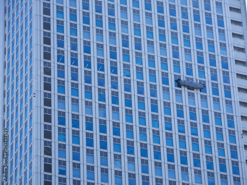 日本の都市の高層オフィスの外壁を掃除するゴンドラに乗る作業員の姿