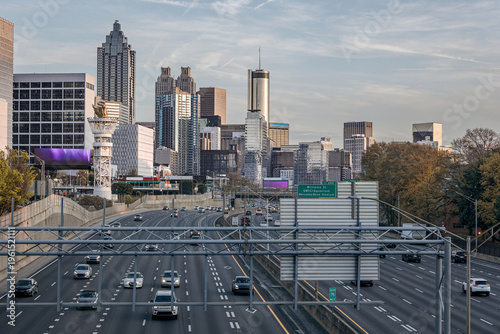 View of the Downtown Atlanta Skyline Cityscape showing several prominent buildings, highways, cars, and hotels on a beautiful clear evening as seen from a city street.
