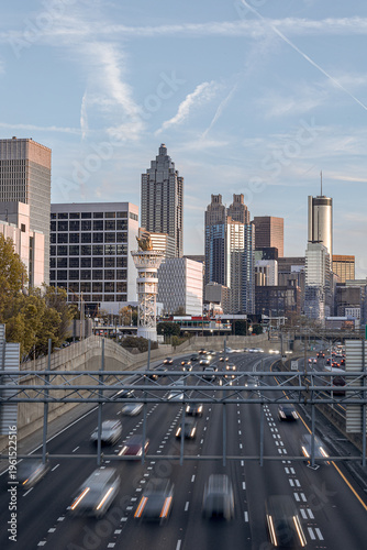 View of the Downtown Atlanta Skyline Cityscape showing several prominent buildings, highways, cars, and hotels on a beautiful clear evening as seen from a city street.
