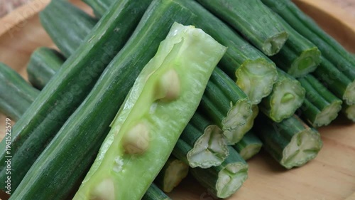 Fresh Moringa pods are arranged on a wooden plate.