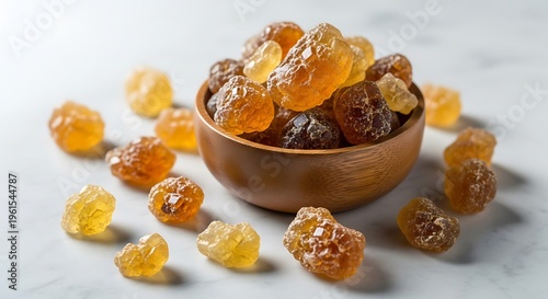 A wooden bowl filled with various pieces of golden amber resin sitting on a white marble surface. acacia gum