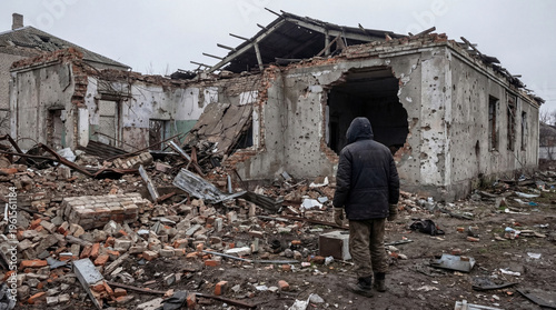 Canvas Print Lone person stands before a extensively damaged house with a gaping hole
