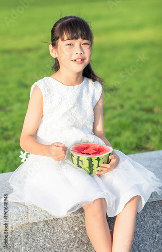 A little Chinese girl eating watermelon in the park during summer