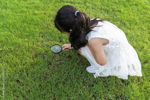 A little Chinese girl playing with a magnifying glass in the park