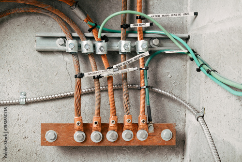 Electrical grounding and bonding busbar system in electrical room.  Labeled grounding rods. Copper conductors, clamps, and grounding electrodes mounted on wall. Selective focus.