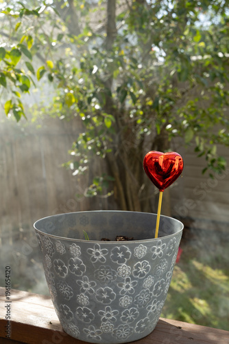 Heart Decoration Stands in a Flower Pot During Daylight With Sunlight Shining Through Trees