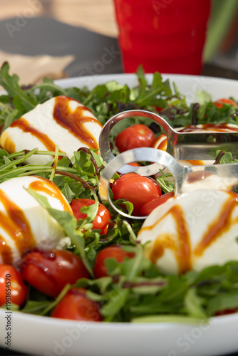 Fresh Salad With Mozzarella Balls and Cherry Tomatoes Served on a Plate in Bright Daylight With a Red Drink in the Background