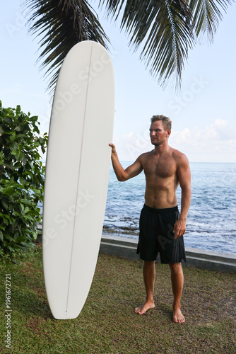 Casual Surfer Showing Shaka By Palm Tree. Beachgoer Demonstrating Aloha Spirit With Longboard Nearby