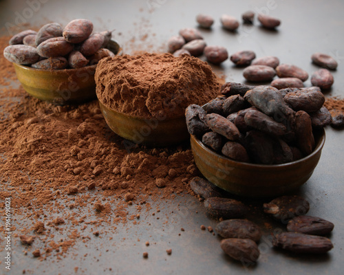 Cocoa beans and a pile of cocoa powder in wooden bowls on a stone table