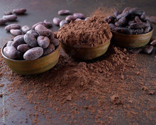 Cocoa beans and a pile of cocoa powder in wooden bowls on a stone table