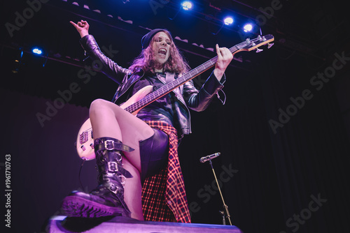 Foto A rocker girl in black leather jacket faces the crowd, screaming and playing heavy rock on her electric guitar under dramatic stage spotlights