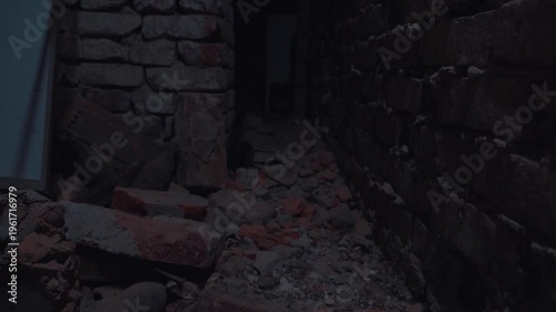 An abandoned brick-walled basement, illuminated by flickering light of a broken lamp. The dirt floor is littered with brick fragments and debris. The scene is dark and eerie. The angle is from below