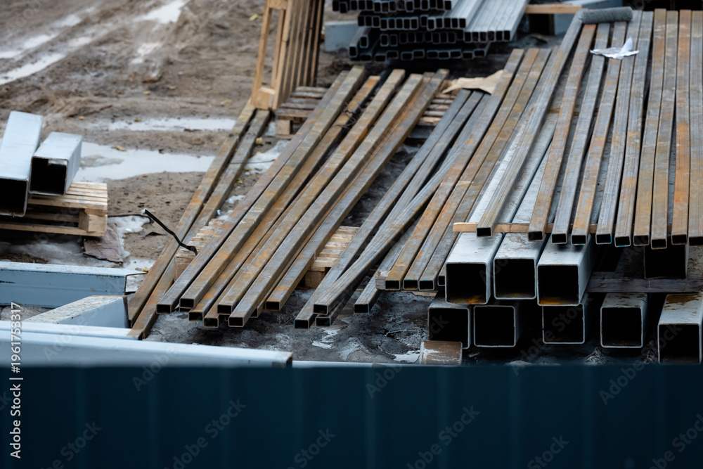 Obraz premium Stacks of steel beams and rectangular metal tubes arranged outdoors on a muddy worksite