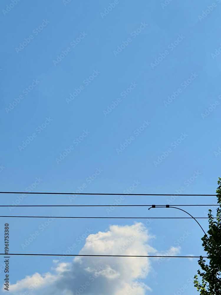 Fototapeta premium Electric power lines under a clear blue sky with white clouds