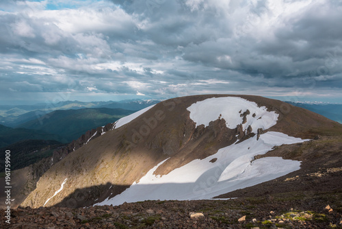 Dramatic view from high stony pass to big stone hill with white snowfield abo...