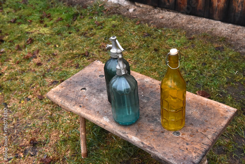 Fotografie Vintage glass soda siphons and yellow bottle on rustic wooden bench