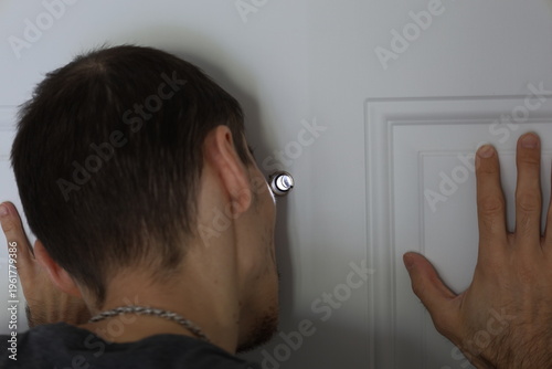 Slika na platnu Man holding a door and looking through peephole, showing caution and awareness
