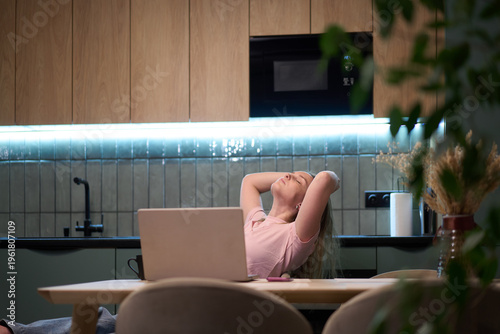 Female leaning back in chair near laptop in kitchen