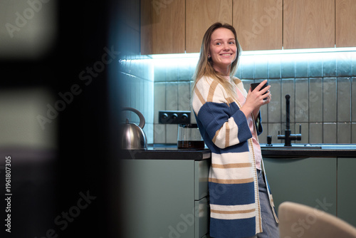Female standing in kitchen holding cup indoors