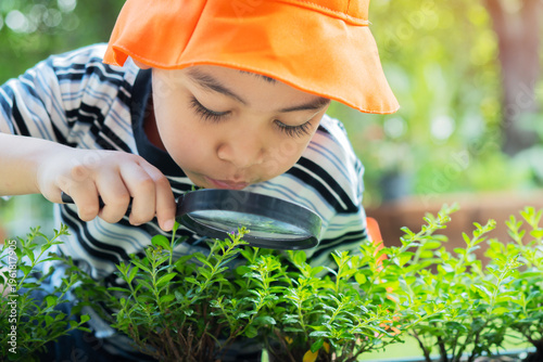Happy little boy wearing orange hat with magnifying glass explorer and learning the nature