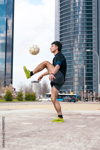 Young athletic man performing freestyle soccer tricks, juggling a football with skill and concentration in an urban environment