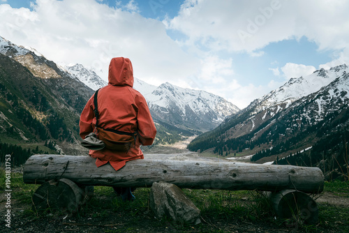 Foto woman in a orange jacket sitting on a bench on a rocky shore on a cloudy day, rear view