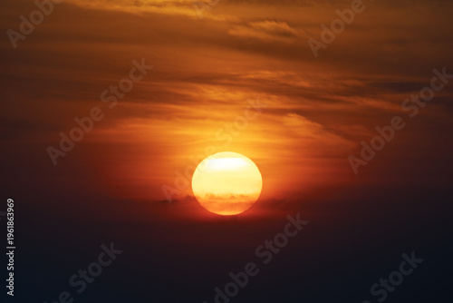 large round orange sunrise or sunset with cloudy sky for background, image shot with super telephoto lens