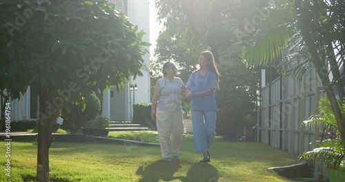 Female caregiver assisting senior woman walking in the garden for therapy.