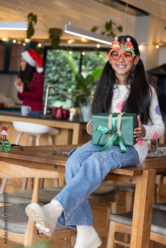 Asian family sharing in kitchen preteen girl wearing novelty glasses holding green gift, copy space