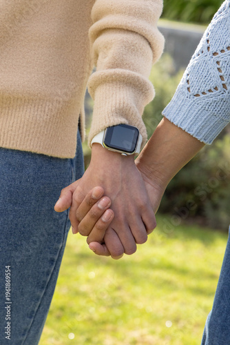 Two people holding hands at waist in garden, wearing knit sweaters and showing smartwatch on wrist