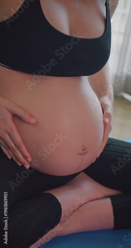 Pregnant woman sitting on a mat and gently massaging her belly.
