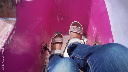 Feet relaxed in casual sandals, paddling a small pink boat on the wavy surface of the water