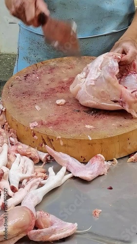 Butcher Using a Sharp Cleaver to Process Raw Fresh Chicken on a Large Wooden Chopping Block