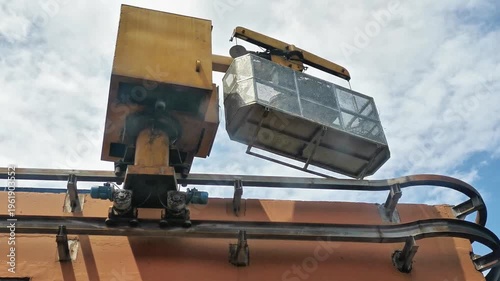 Industrial crane lifting metal work platform basket at construction site under cloudy sky