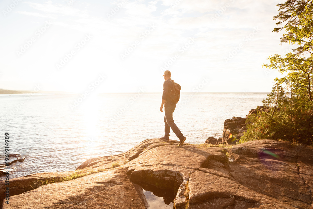 Naklejka premium Hiking, travel and back with man in nature for trekking adventure, backpacking and seaside space. Walking, summer vacation and sunshine with person or hiker outdoor for ocean, explore and tourism
