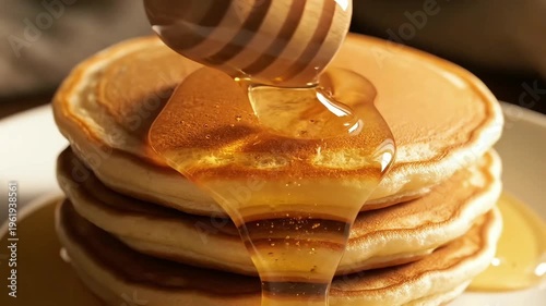 Extreme close-up of golden honey pouring from a wooden dipper onto a stack of fresh fluffy pancakes in warm morning light.