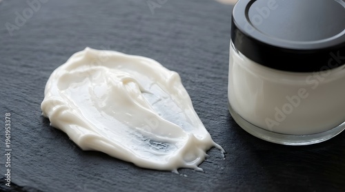 A smear of white cream on a dark surface next to a small glass jar