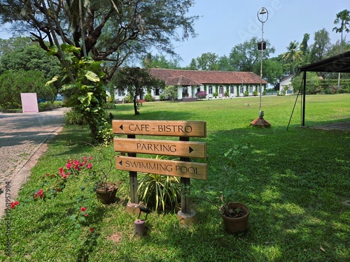 Foto A quaint wooden signpost in Fort Kochi stands on a lush lawn, pointing the way to a Cafe-Bistro, Parking, and Swimming Pool