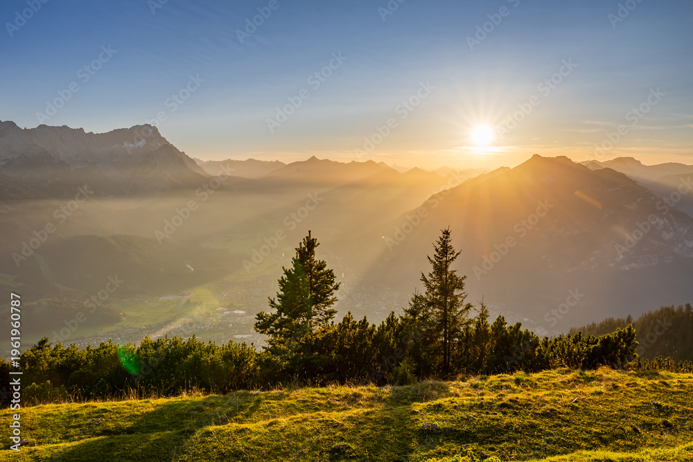 Obraz premium Suset over mountains with a view of the valley and forest in the foreground. The sky shows warm colors as day ends.