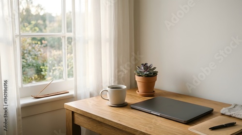 A wooden desk with a laptop, mug, and potted plant near a window with white curtains