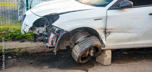 Car with damaged front end and missing tire in urban setting during daylight hours