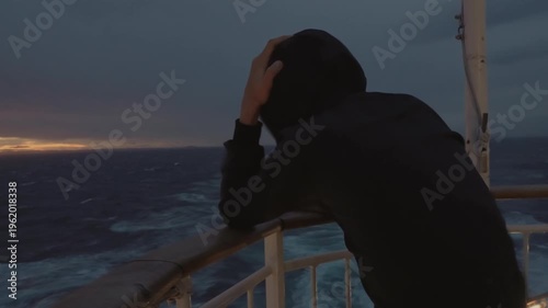 Boy in a hooded jacket on the aft deck, braving wind and waves on the ferry from Copenhagen to Oslo. An authentic, emotional moment during a rough weather sunset in Scandinavia.
