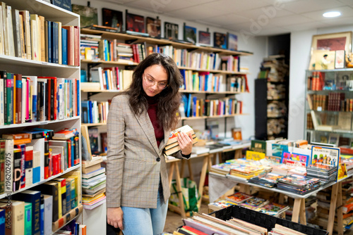 Foto Young woman browsing shelves and holding books in a cozy independent bookshop