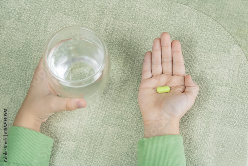 A child's hand holding a yellow pill and a glass of water. close-up analgesic for abdominal pain, headache, pain syndrome for treatment, medication or vitamins.
